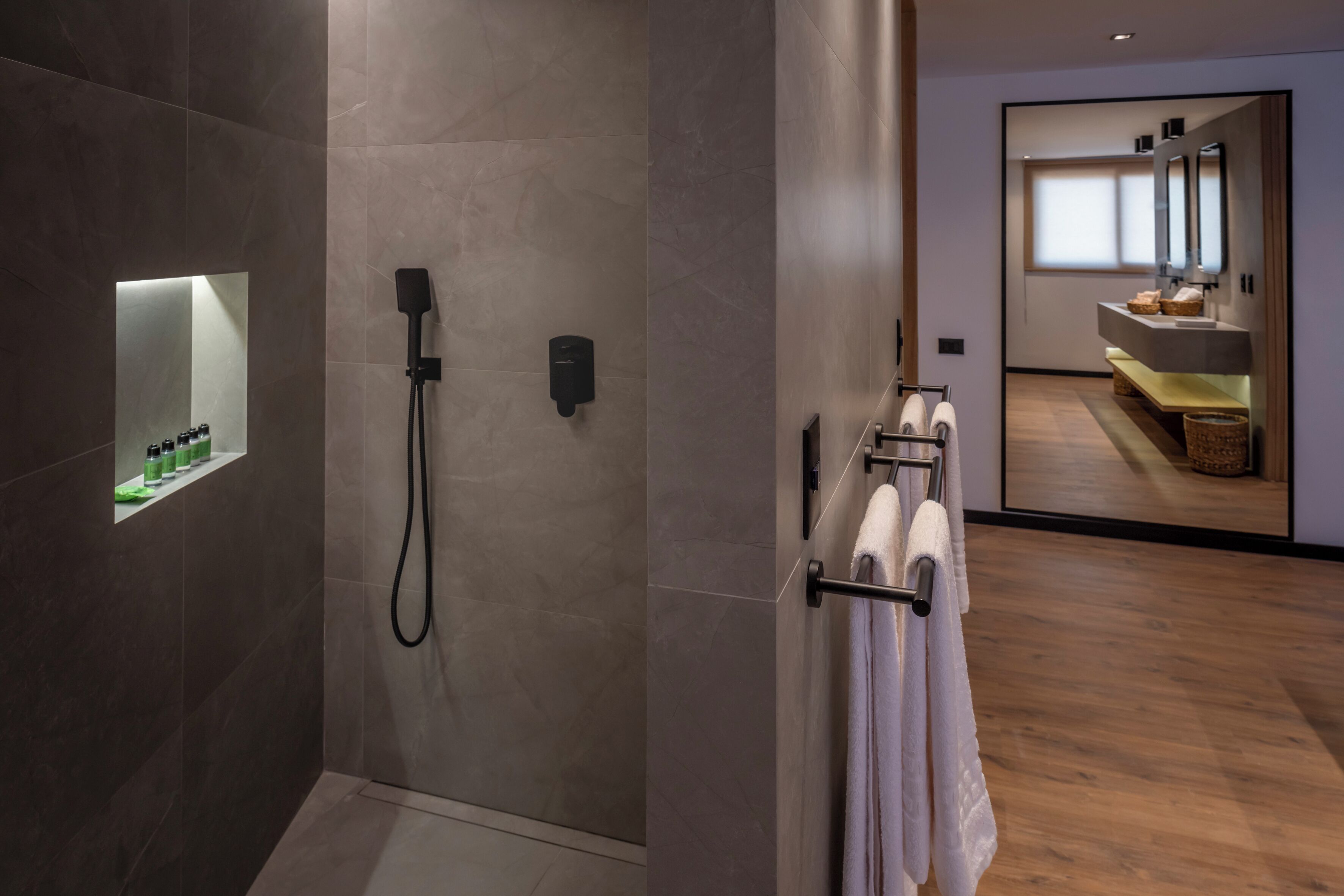 A modern bathroom with a glass-enclosed shower, a towel rack with white towels, and a large mirror above the sink.