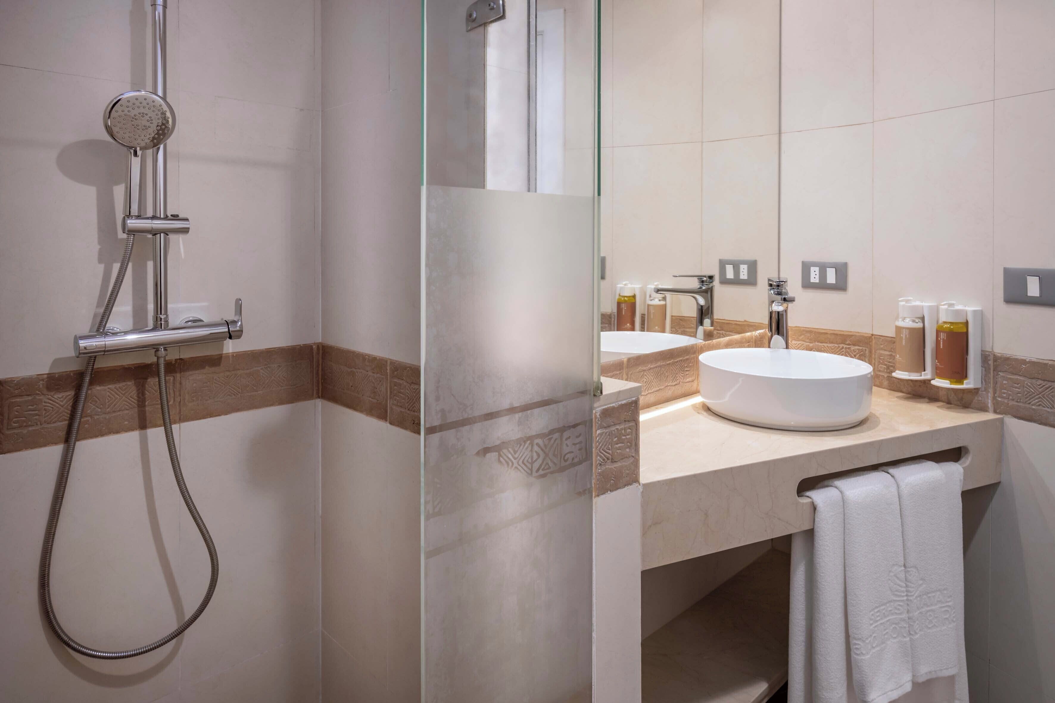 Un baño moderno con cabina de ducha de vidrio, un lavamanos redondo y un perchero para toallas.