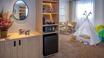 A compact room with a kitchenette, a mirror, a small refrigerator, a bookshelf, a dining area, a tent, and a children's play area.