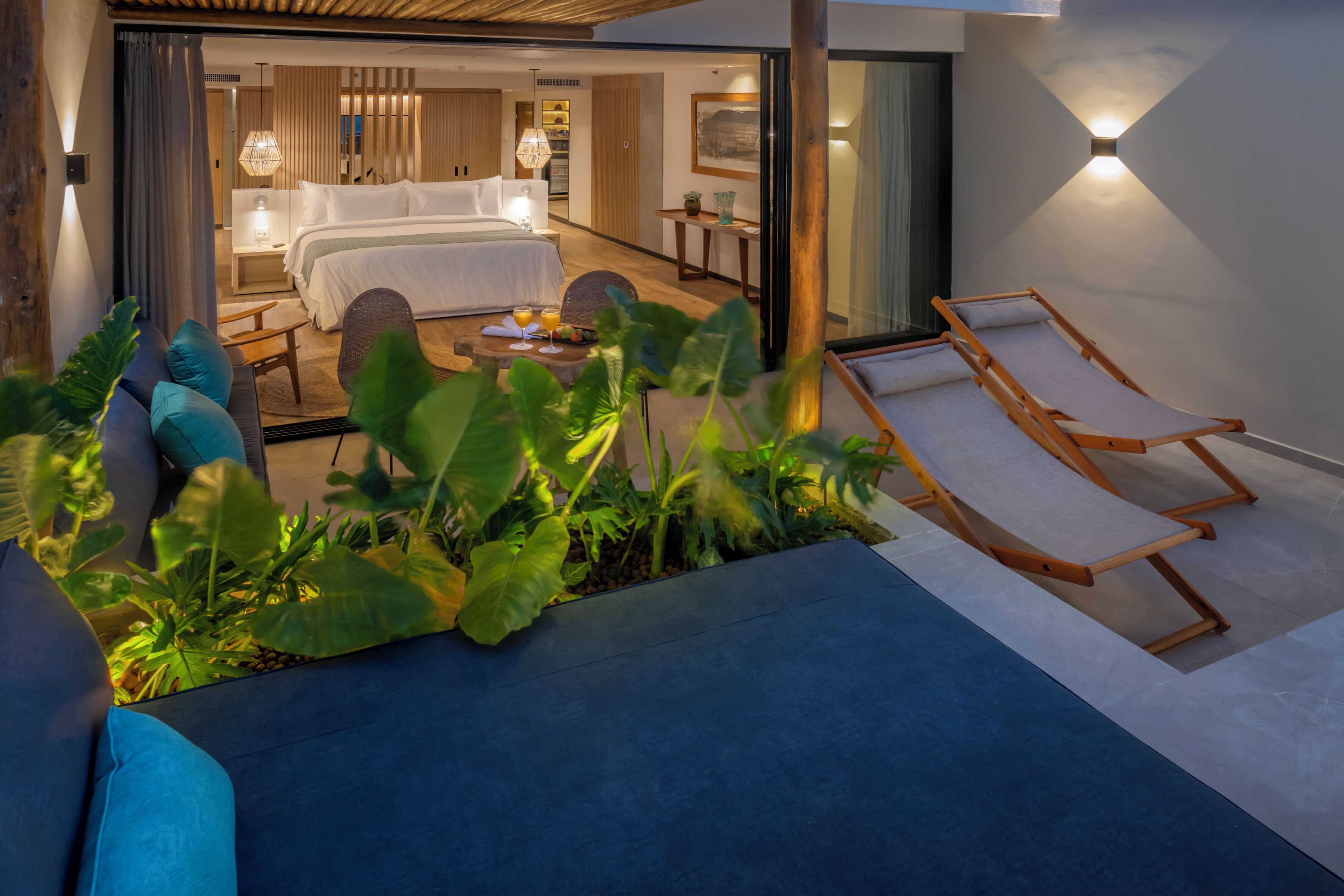 Et moderne hotelværelse med en stor seng, et opholdsområde med sofabord og en balkon med liggestol.