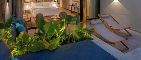 A modern hotel room with a large bed, a sitting area with a coffee table, and a balcony with a lounge chair.