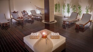 A spa room with wooden flooring, lounge chairs, a bed with towels, and a central pillar. - Serhs Natal Grand Hotel & Resort (Natal)
