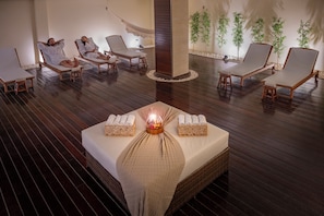 A spa room with wooden flooring, lounge chairs, a bed with towels, and a central pillar. - Serhs Natal Grand Hotel & Resort (Natal)