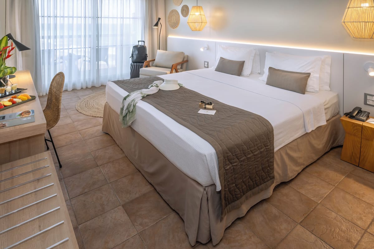 A modern hotel room with a large bed, a desk with a laptop, a chair, and a suitcase.