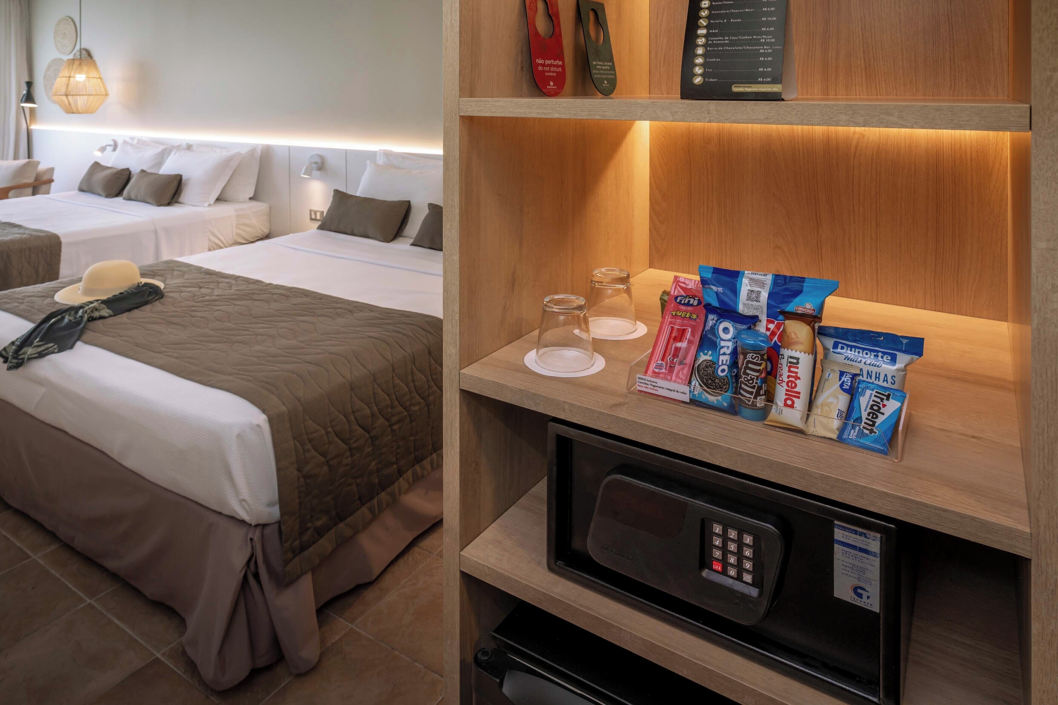 A hotel room with two beds, a microwave, and a shelf with snacks.