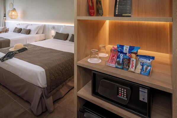 A hotel room with two beds, a microwave, and a shelf with snacks.