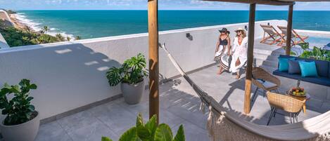 A rooftop terrace with a view of the ocean, potted plants, and outdoor seating.