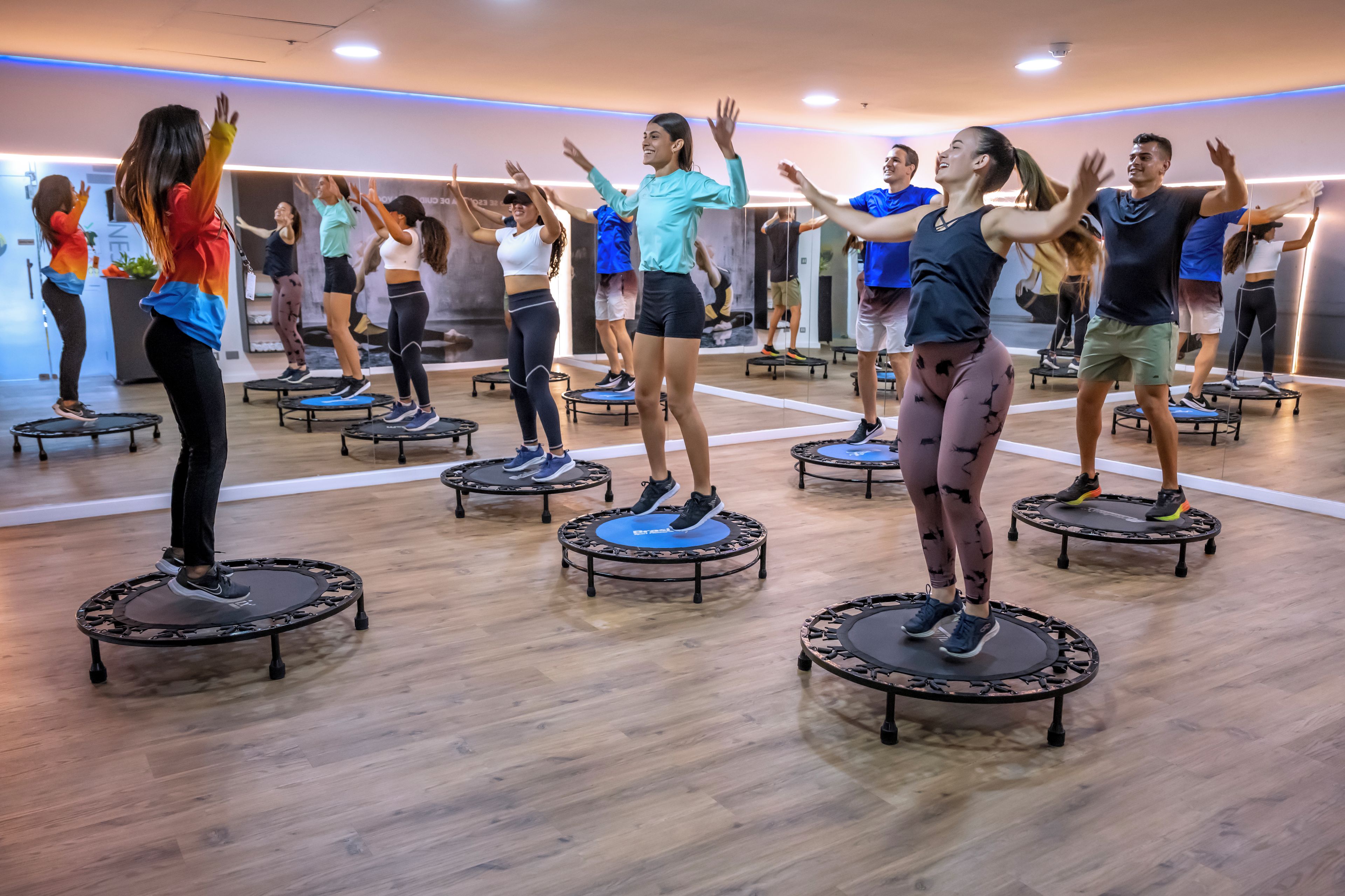 Un grupo de personas haciendo ejercicio en mini trampolines en un gimnasio con suelos de madera y paredes espejadas.