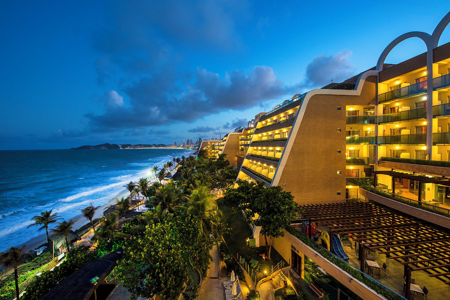 Un hotel con varios balcones con vistas al océano, un área de piscina y vista a la playa.