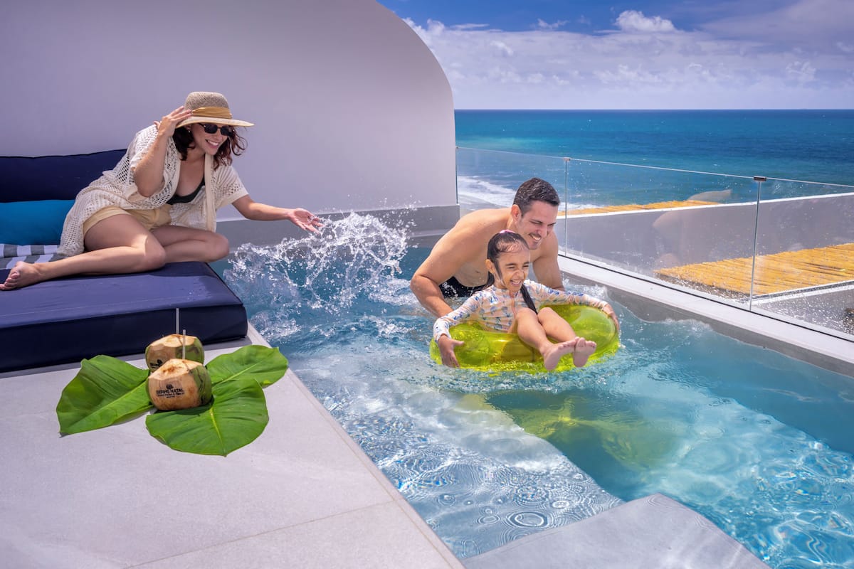 A pool area with a view of the ocean, lounge seating, and a tropical drink setup.