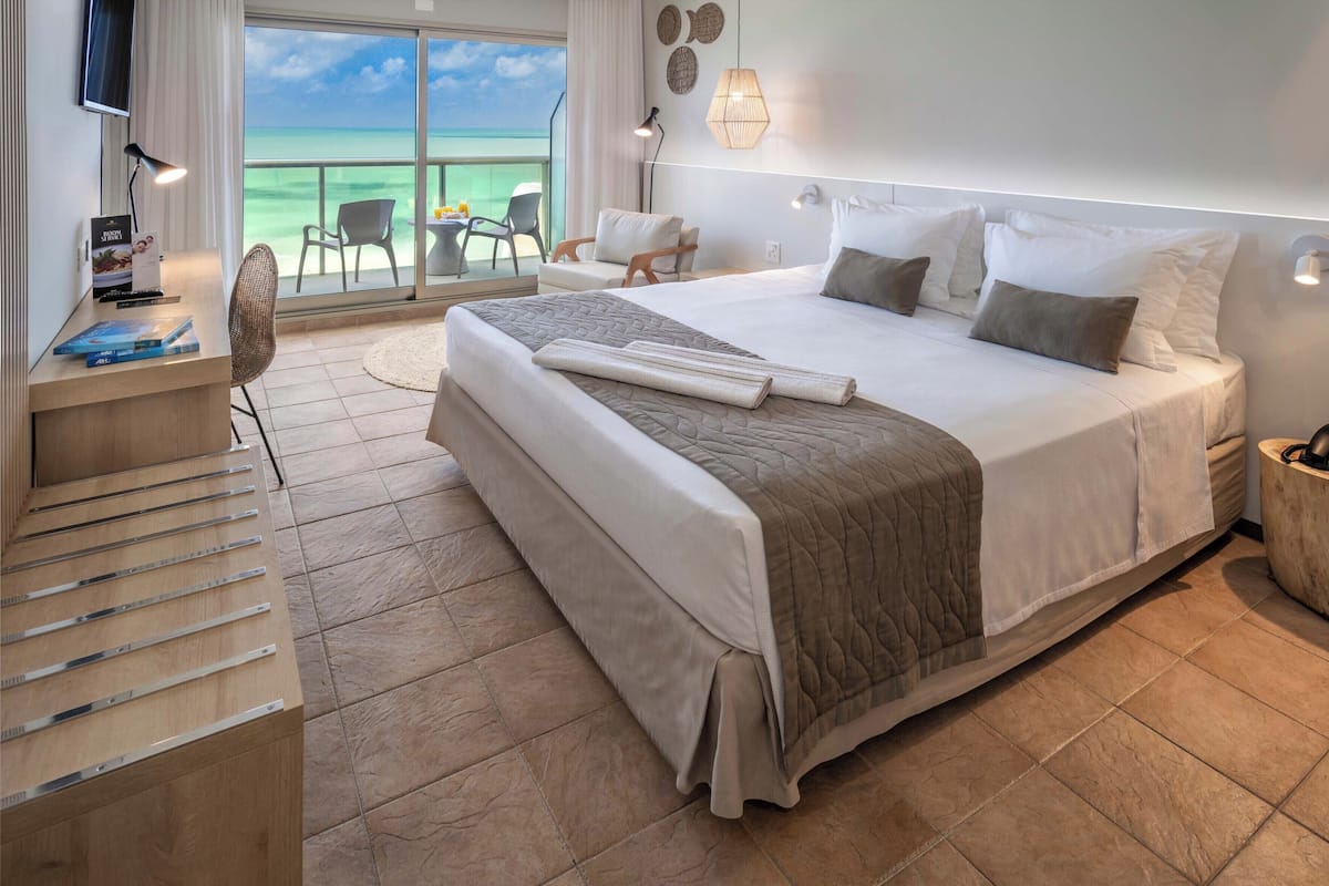 A hotel room with a large bed, a desk with a lamp, a chair, and a view of the ocean.