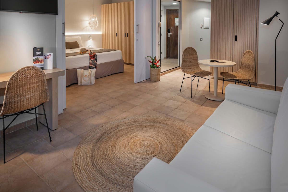A modern hotel room with a bed, a desk, a dining area, and a living space.
