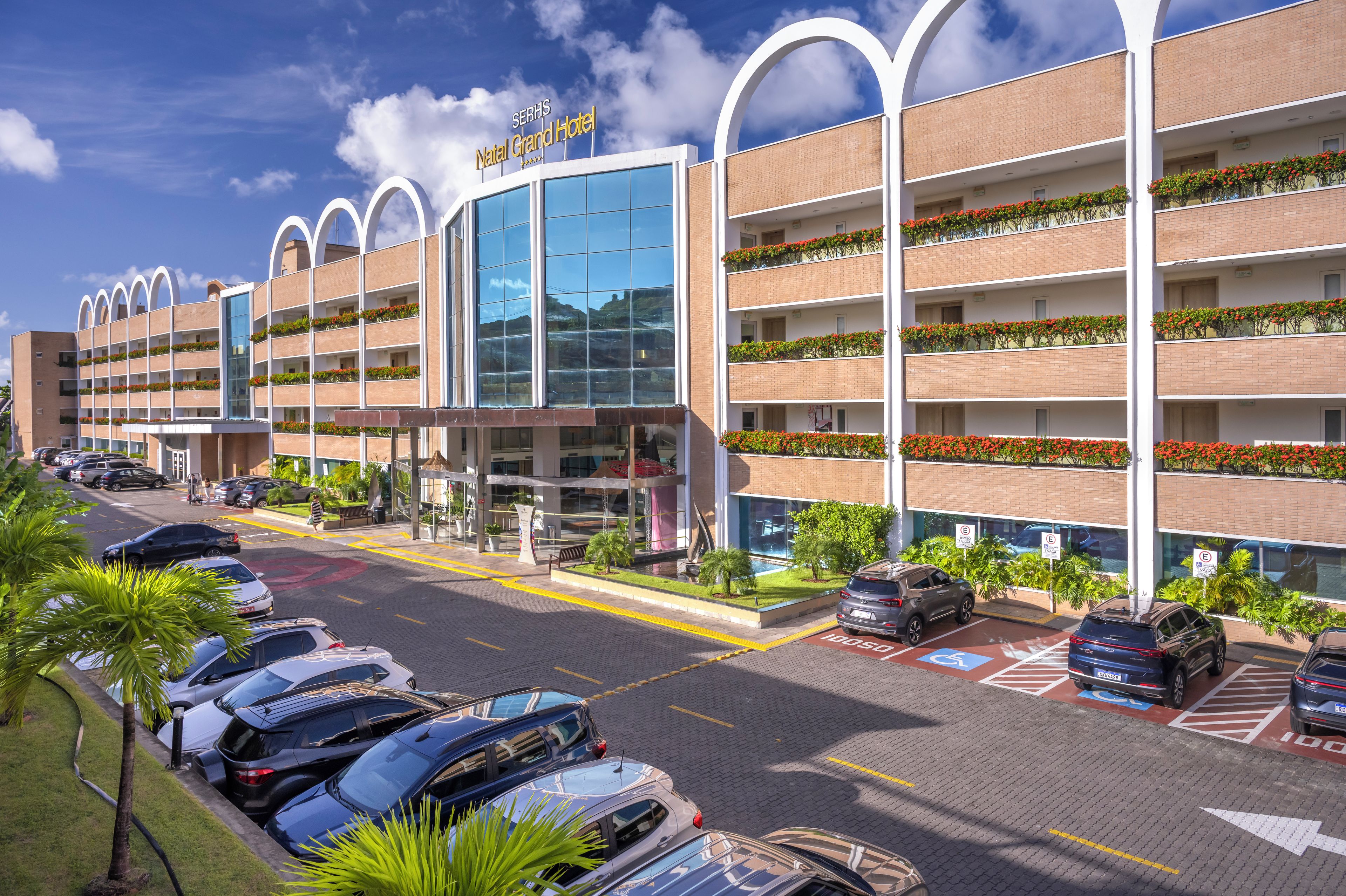 Um hotel com vários andares, design moderno e um estacionamento com diversos carros.