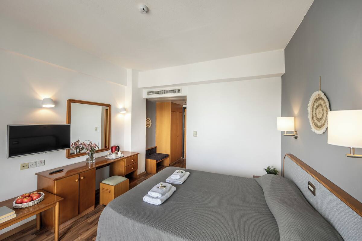 Une chambre d’hôtel équipée d’un lit, d’un bureau, d’une télévision, d’un miroir et d’une armoire.
