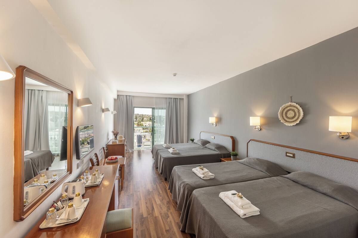 Une chambre d’hôtel avec deux lits, un bureau avec une chaise, un miroir et une vue sur l’extérieur.