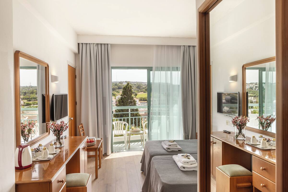 Une chambre d’hôtel avec un balcon, un lit, un bureau, une chaise et un miroir.