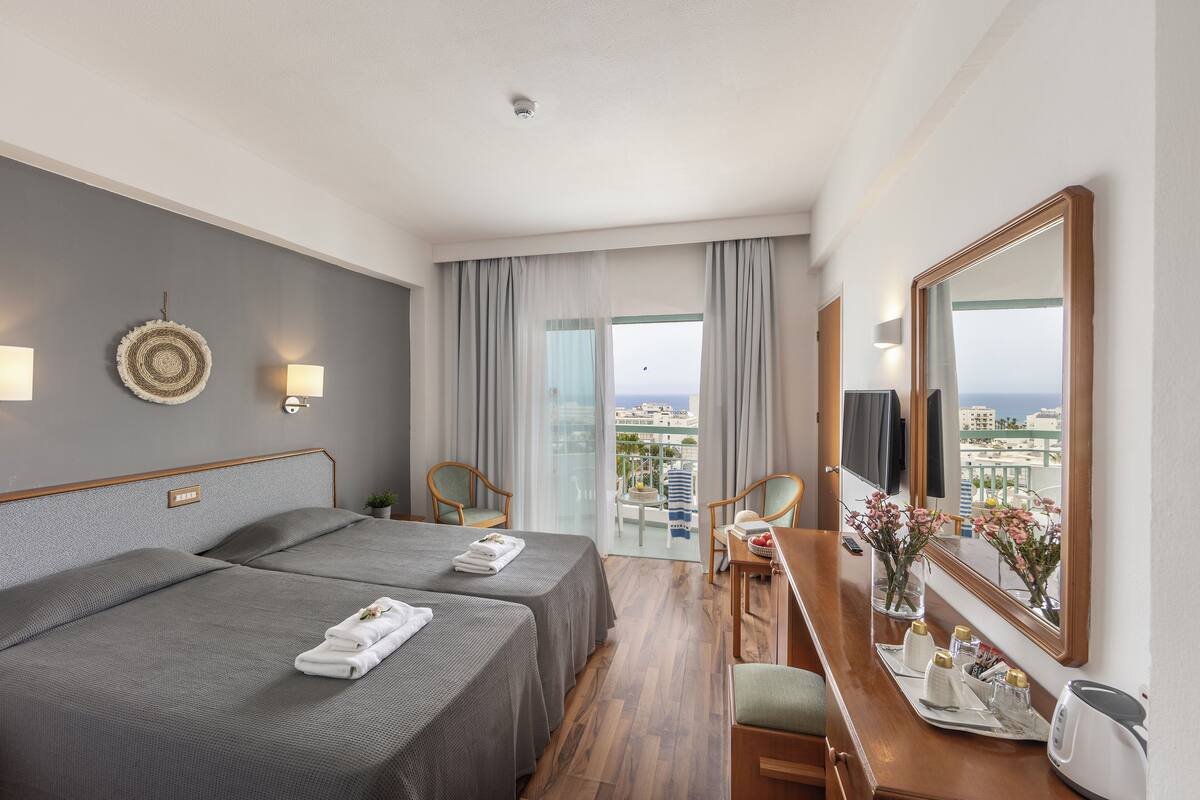 Une chambre d’hôtel avec deux lits, un bureau, une chaise, un miroir et une vue sur la ville.