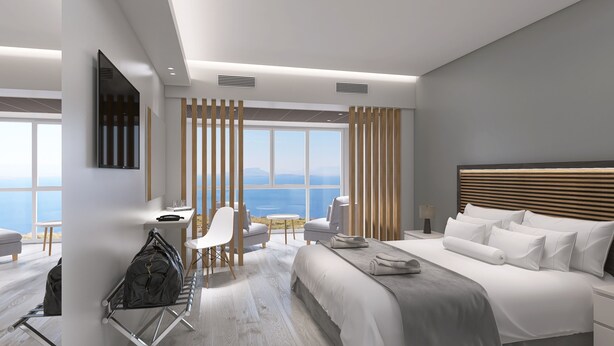 A modern hotel room with a large bed, a desk, and a view of the sea. - Antigoni Hotel (Paralimni)
