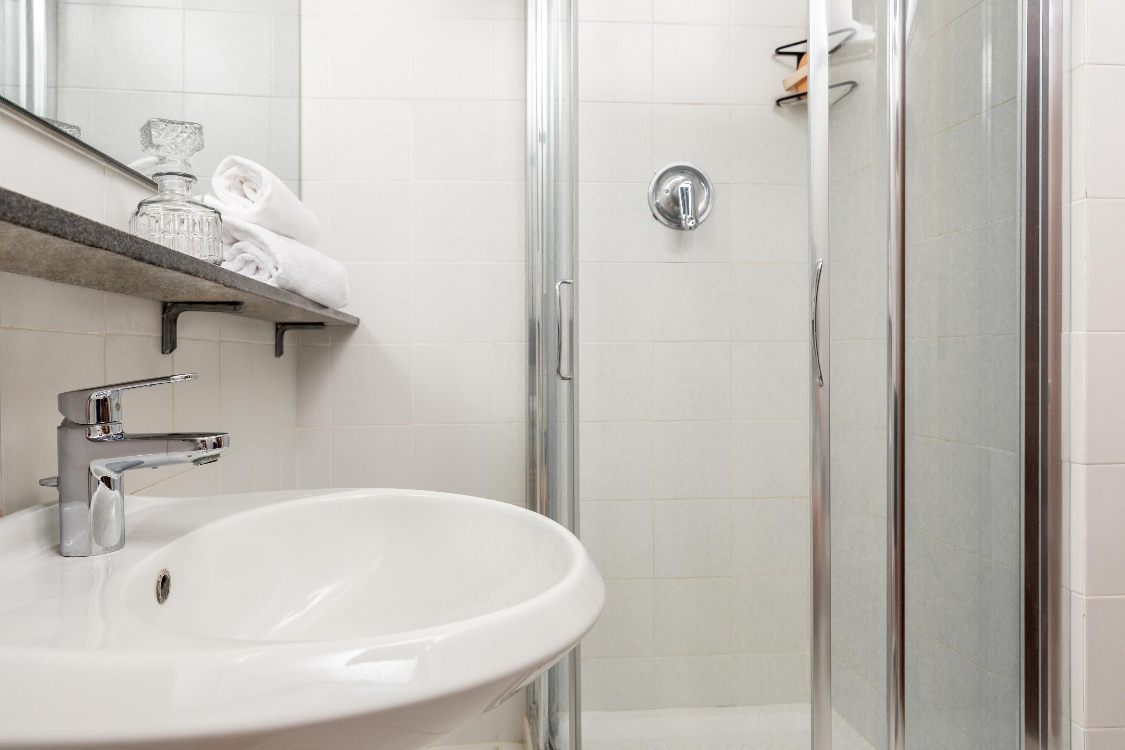Baño con lavamanos blanco, grifo cromado y cabina de ducha con mampara de vidrio.