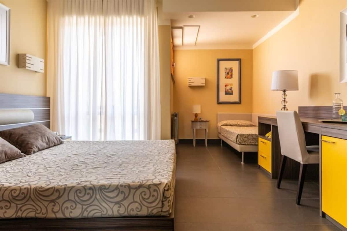 Una camera d'albergo con un letto, una scrivania, una sedia, un tavolino e un quadro appeso al muro.