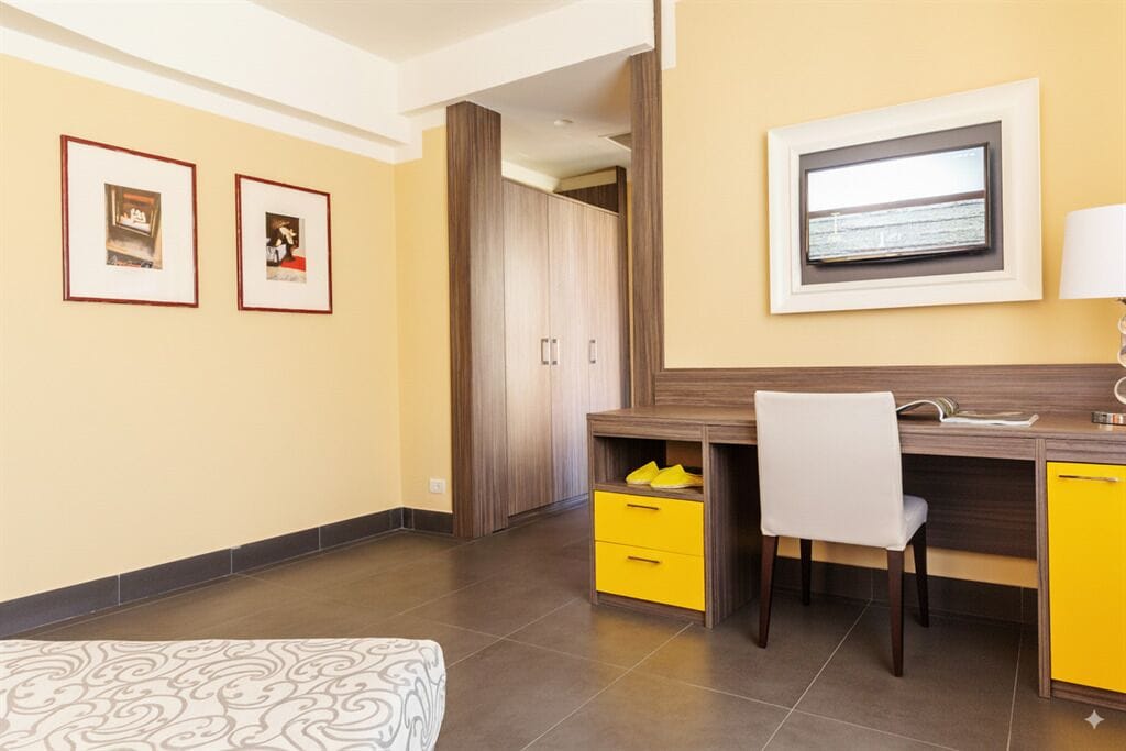A modern room with a desk, chair, and a bed. There are framed pictures on the wall and a window with a view.