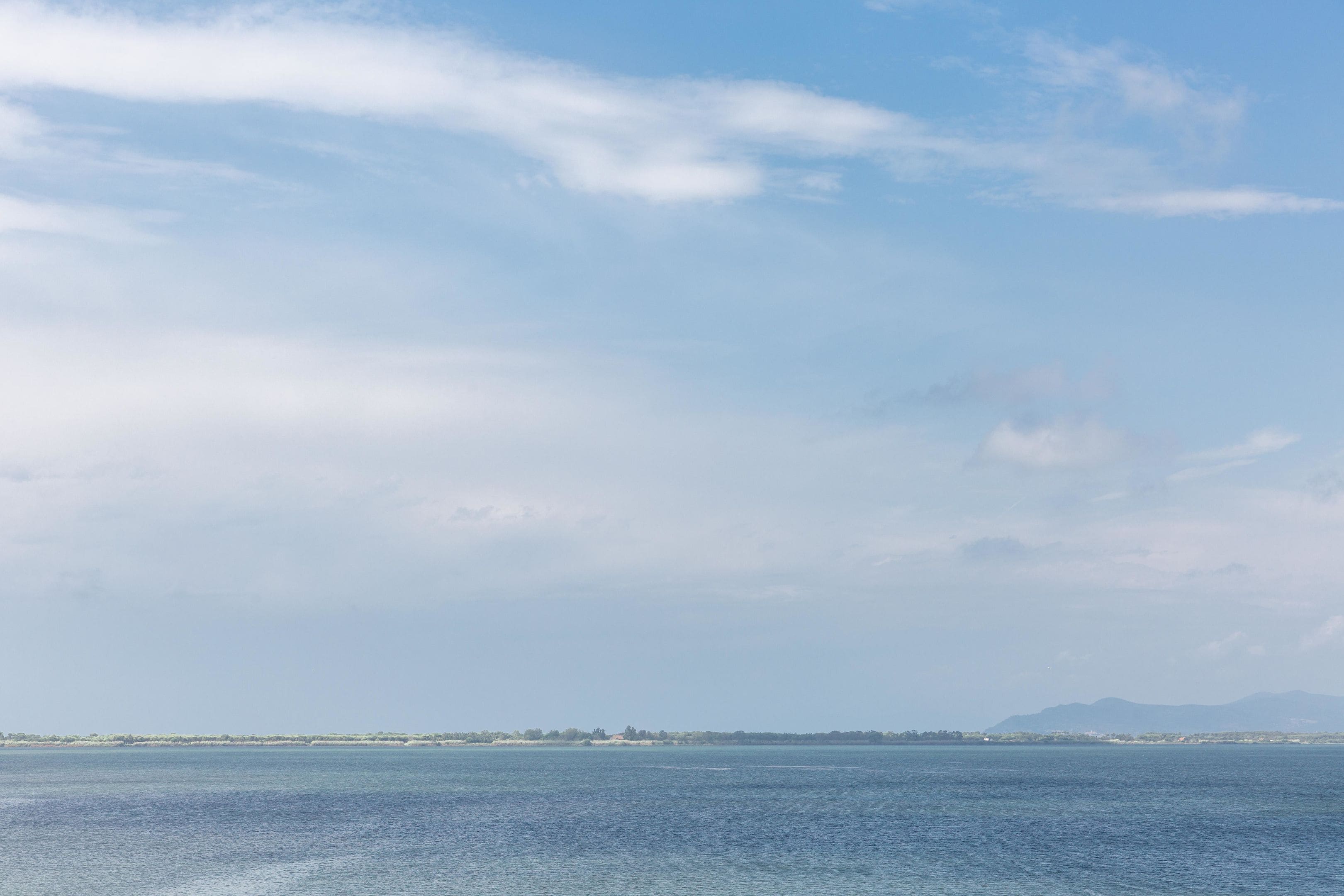 A coastal view with a calm sea, distant land, and a clear sky.