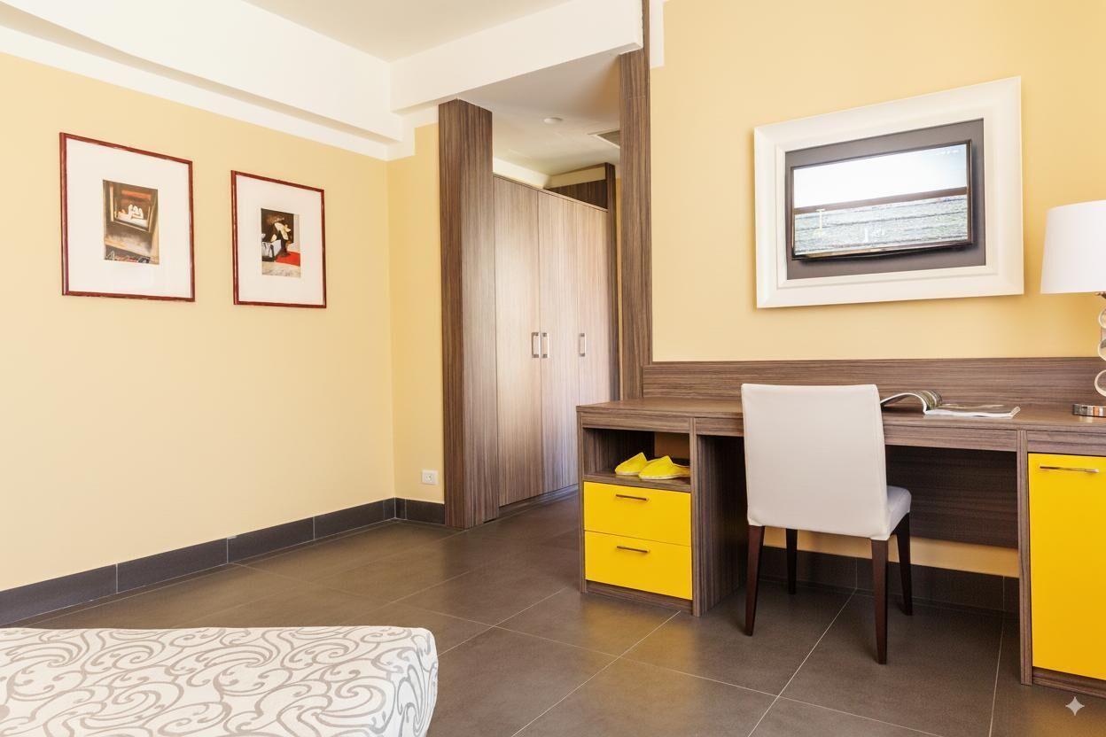 A bedroom with a bed, a desk with a chair, a wardrobe, and two framed pictures on the wall.