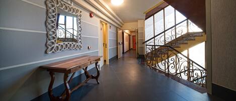 A hallway with a bench, a decorative mirror, and a staircase with wrought iron railings.