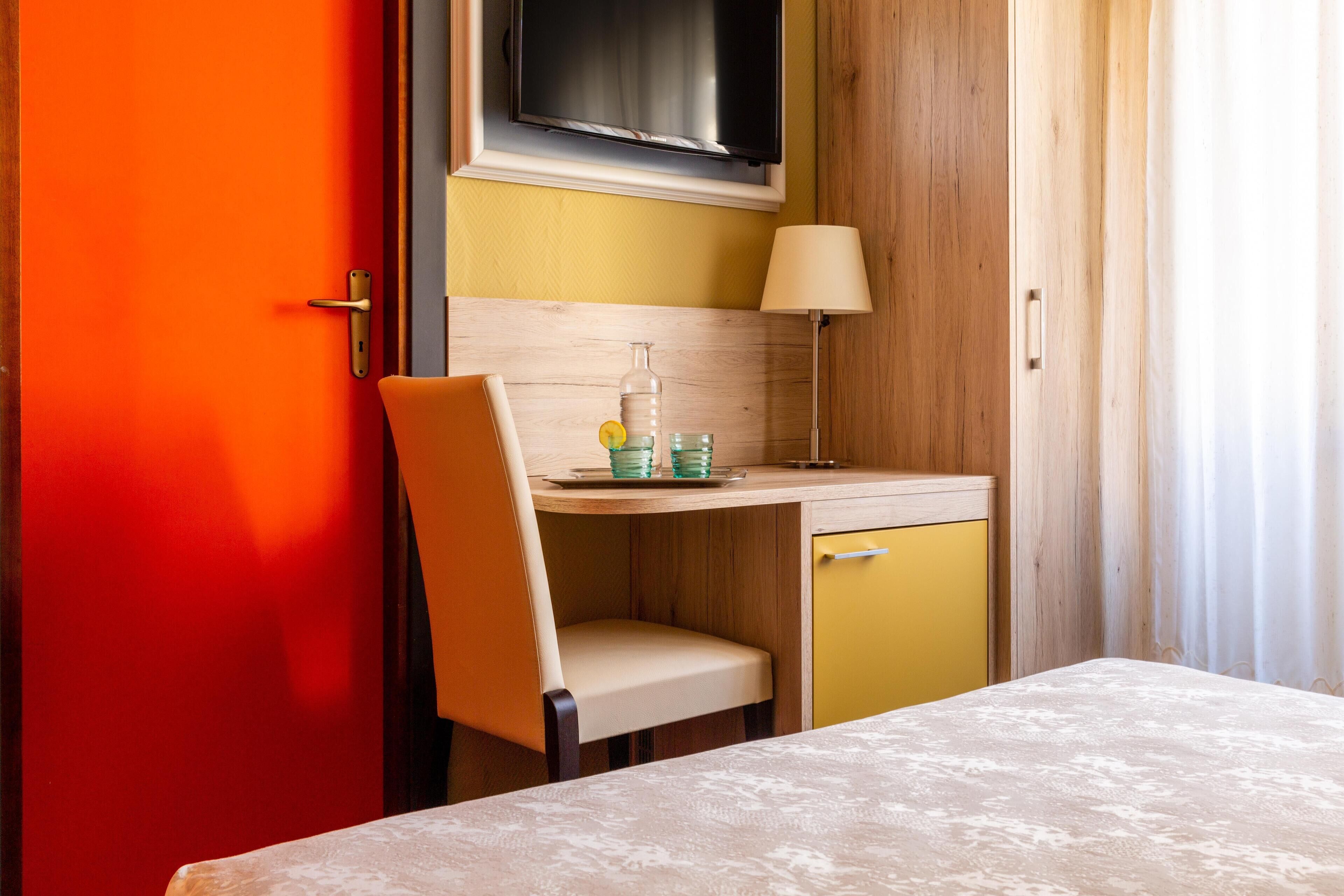 Ein Zimmer mit einem Bett, einem Schreibtisch mit Stuhl, einem darüber montierten Fernseher und einer Lampe.