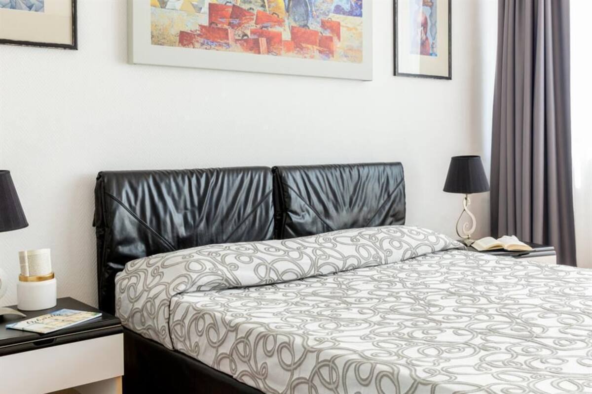 Una camera d'hotel con un letto, un comodino, una lampada e un quadro appeso al muro.