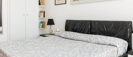 Ein ordentlich eingerichtetes Schlafzimmer mit einem Bett, einem Nachttisch, einer Lampe und einem Bücherregal.