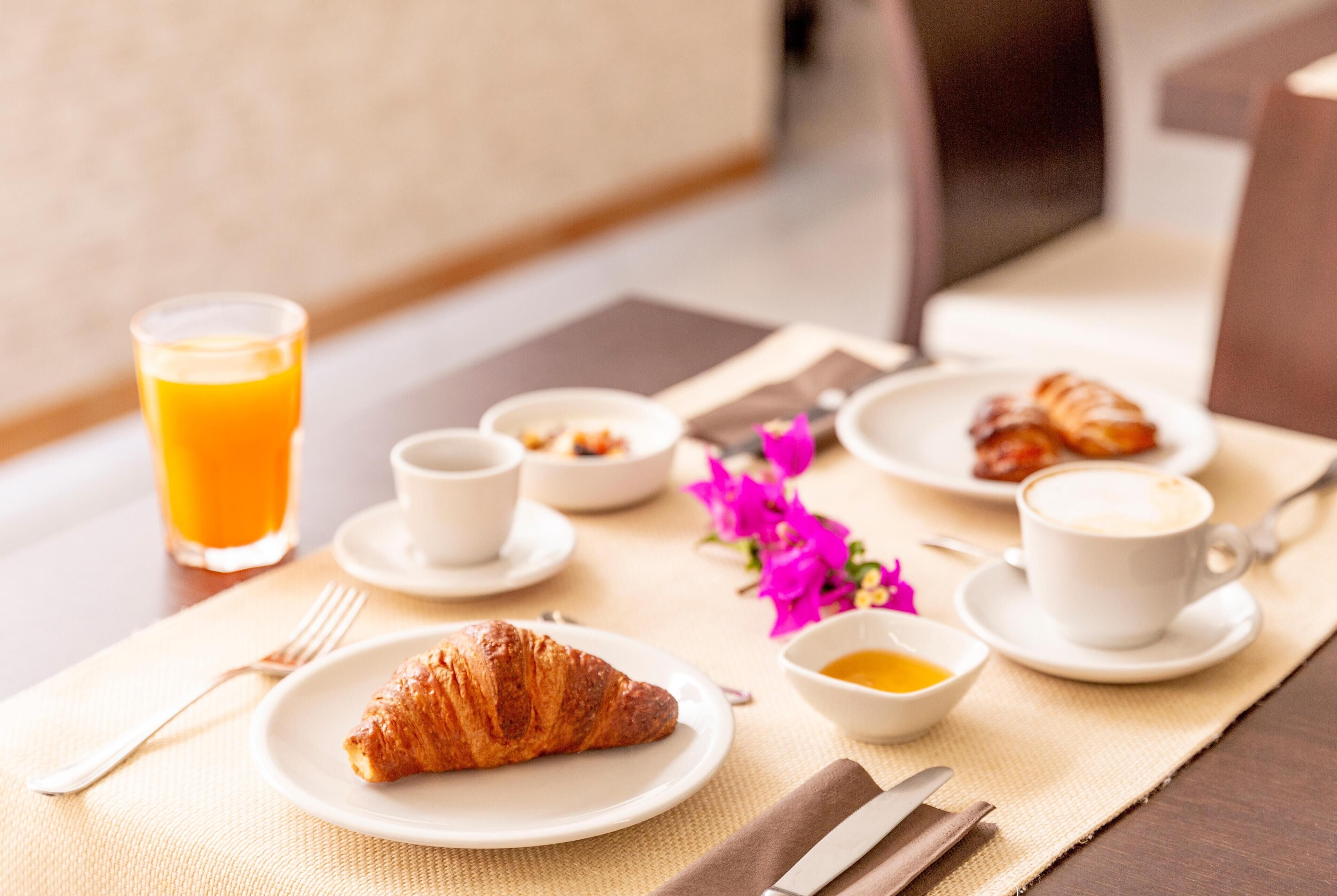 A breakfast setting with croissants, coffee, and orange juice on a table.