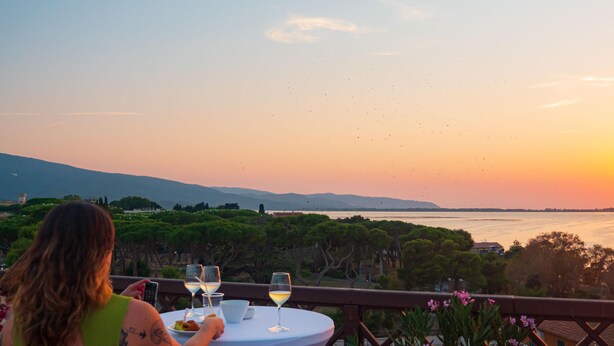 A woman dining at a table with a view of the sunset over a body of water.
