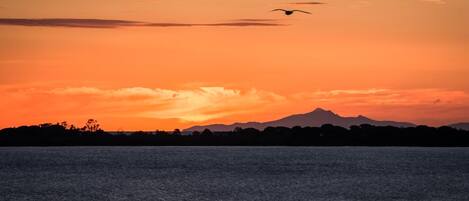 A sunset over a body of water with silhouettes of trees and mountains in the background.
