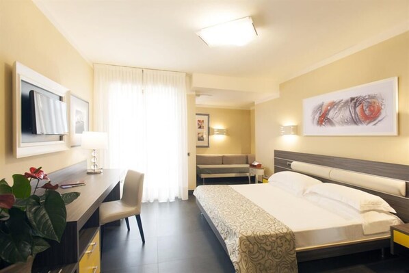 A hotel room with a bed, desk, chair, and artwork on the walls.