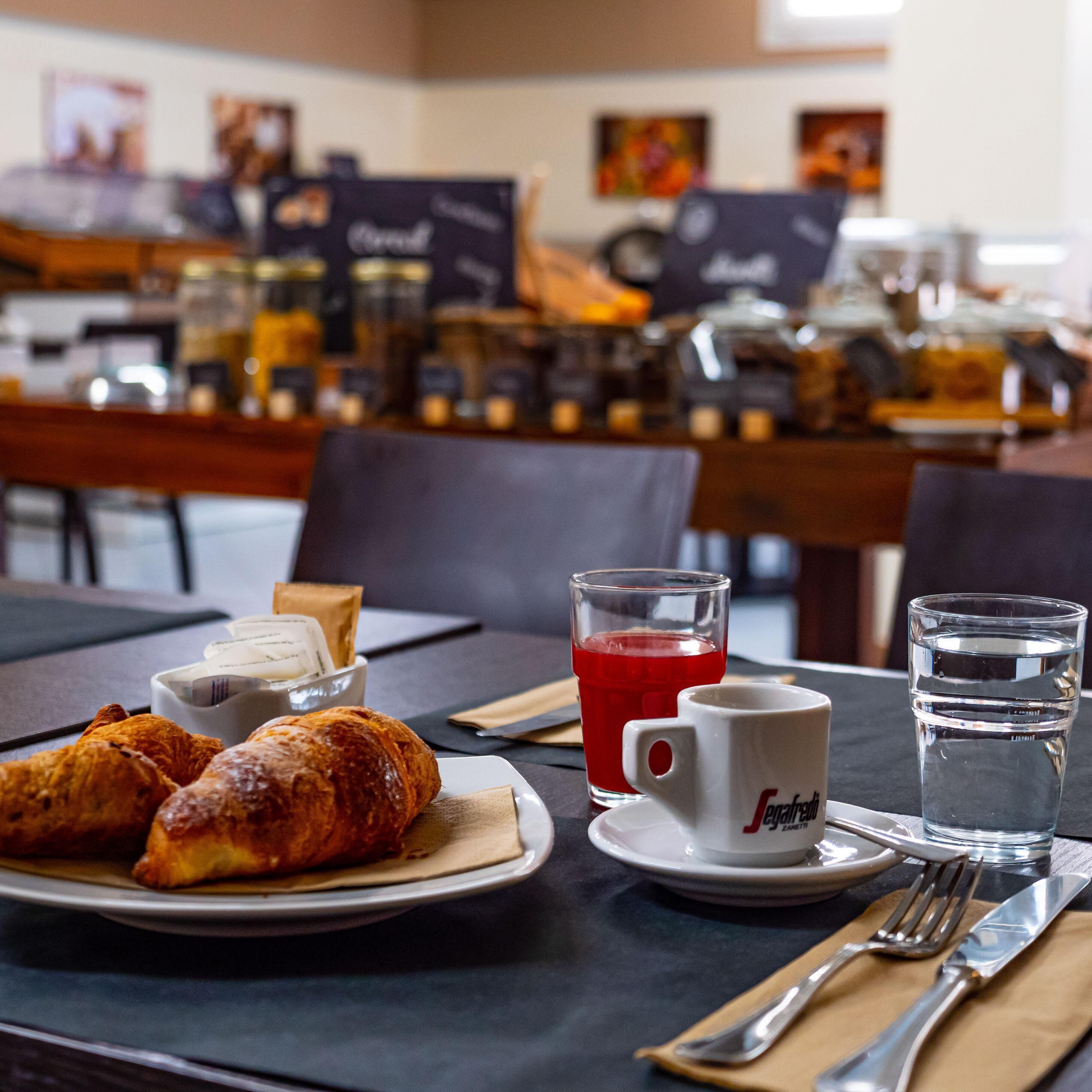A breakfast setting with croissants, a red beverage, and a water glass on a table.