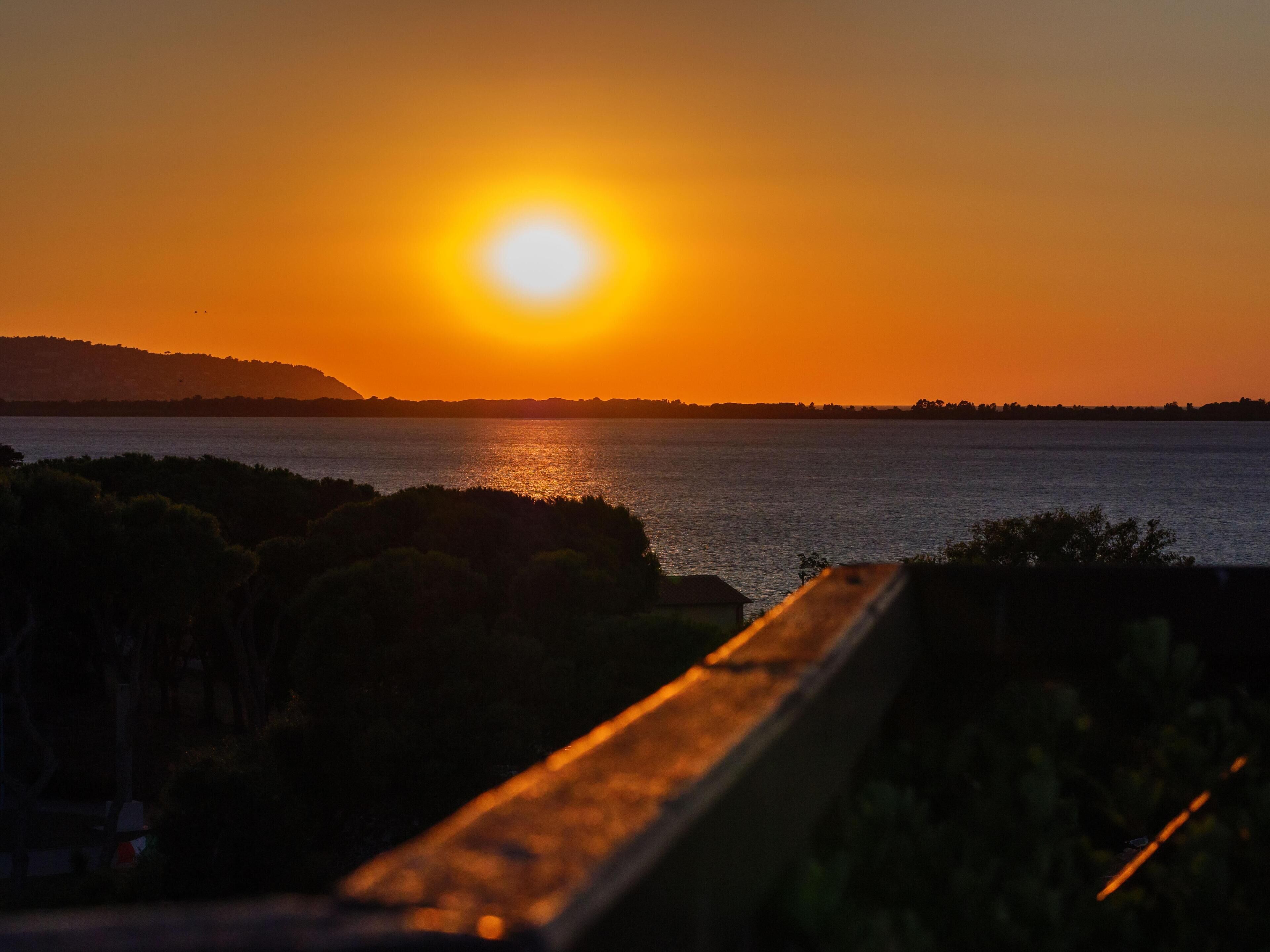 A sunset over a body of water with a distant shoreline and a bridge in the foreground.
