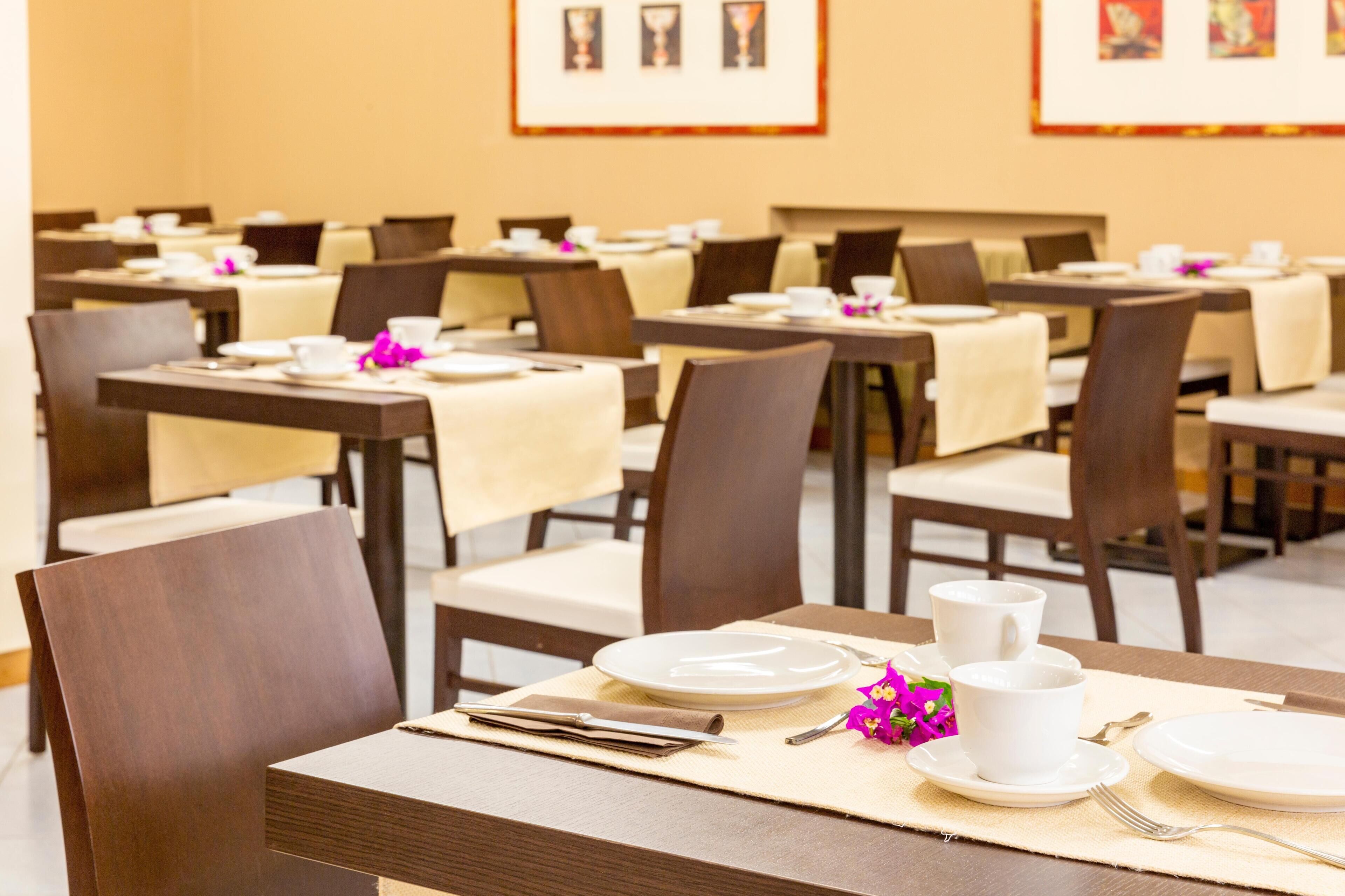 A dining area with tables set for service, chairs, and framed artwork on the walls.