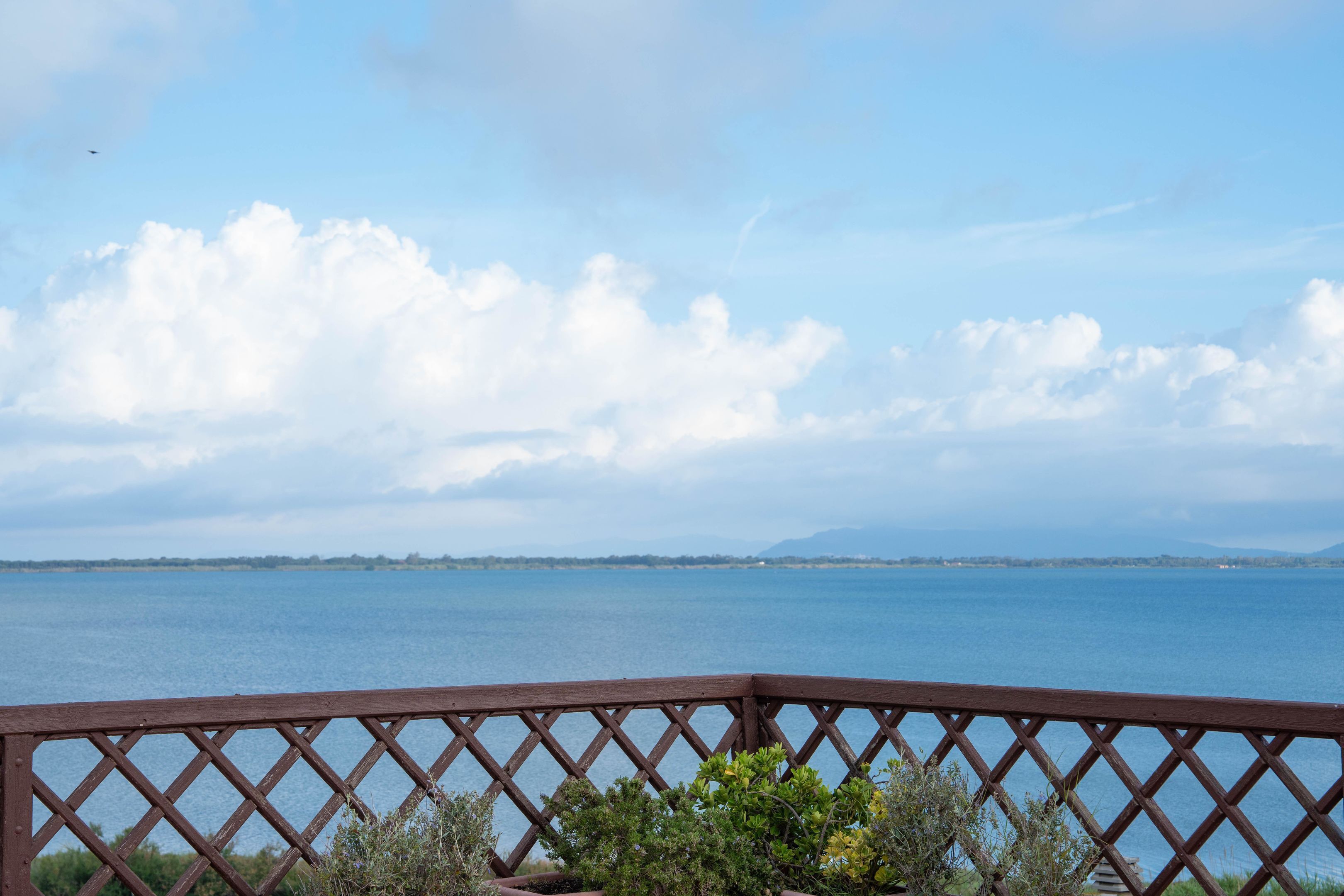 A view of a lake from a wooden deck with a lattice railing, surrounded by greenery.