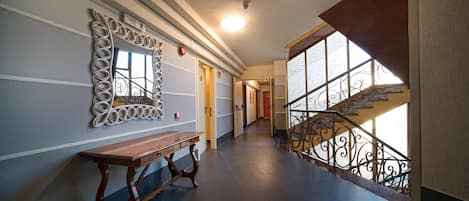 A hallway with a wooden bench, a decorative mirror, and a staircase with wrought iron railings.