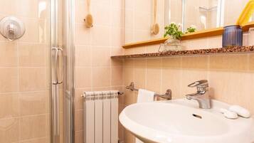 Un baño con cabina de ducha de vidrio, un lavabo blanco con grifo plateado y una pared revestida de baldosas color beige.