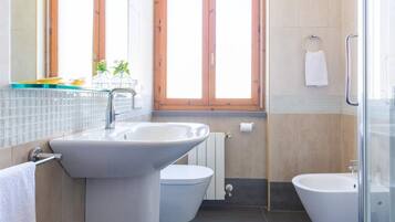 Een moderne badkamer met een wastafel, toilet, bidet en een douchecabine met glazen wanden.