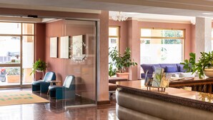 A hotel lobby with a reception desk, seating area, and large windows.