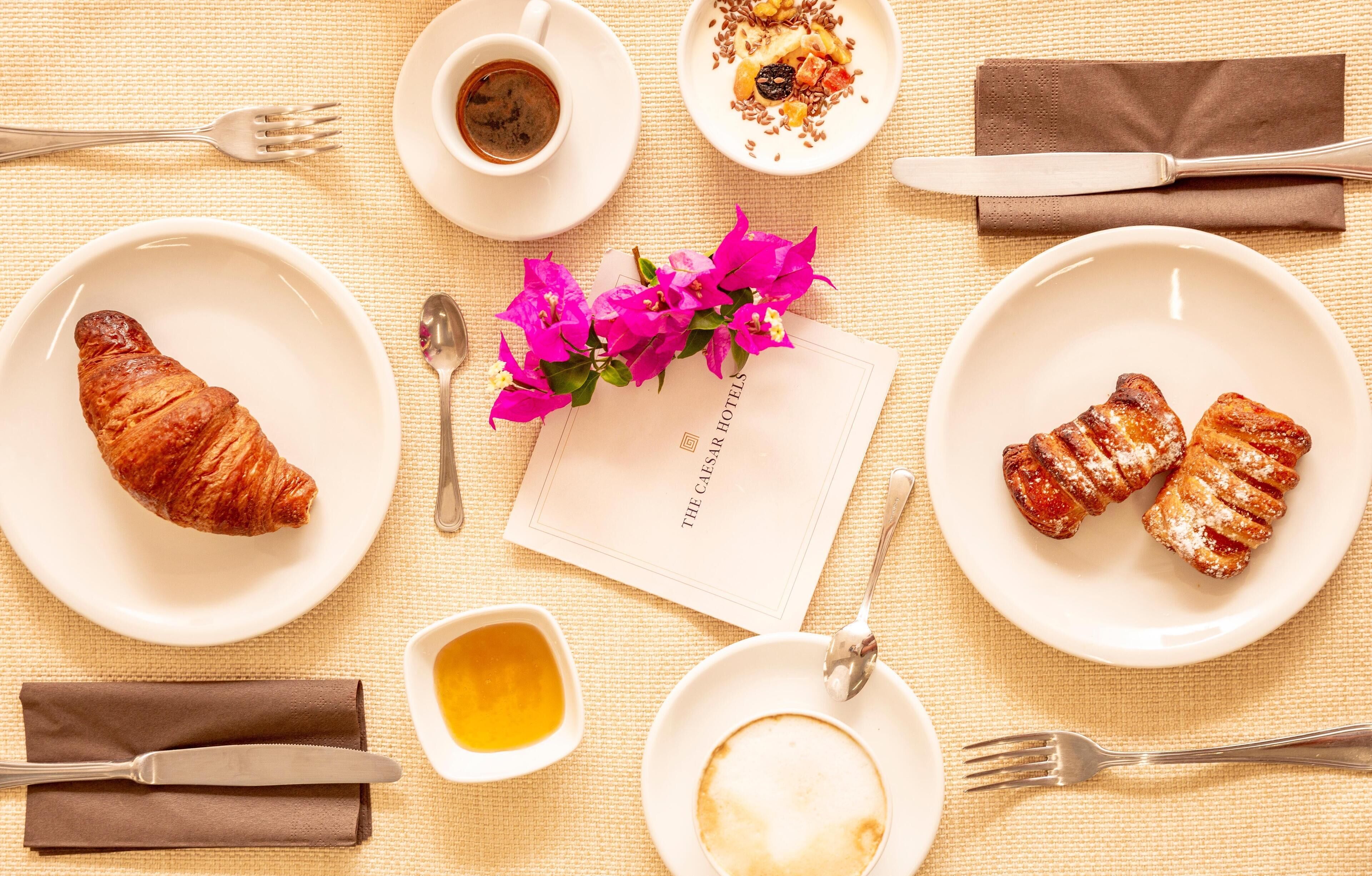 Una escena de desayuno con cruasanes, una taza de café, un plato de postre y una servilleta.