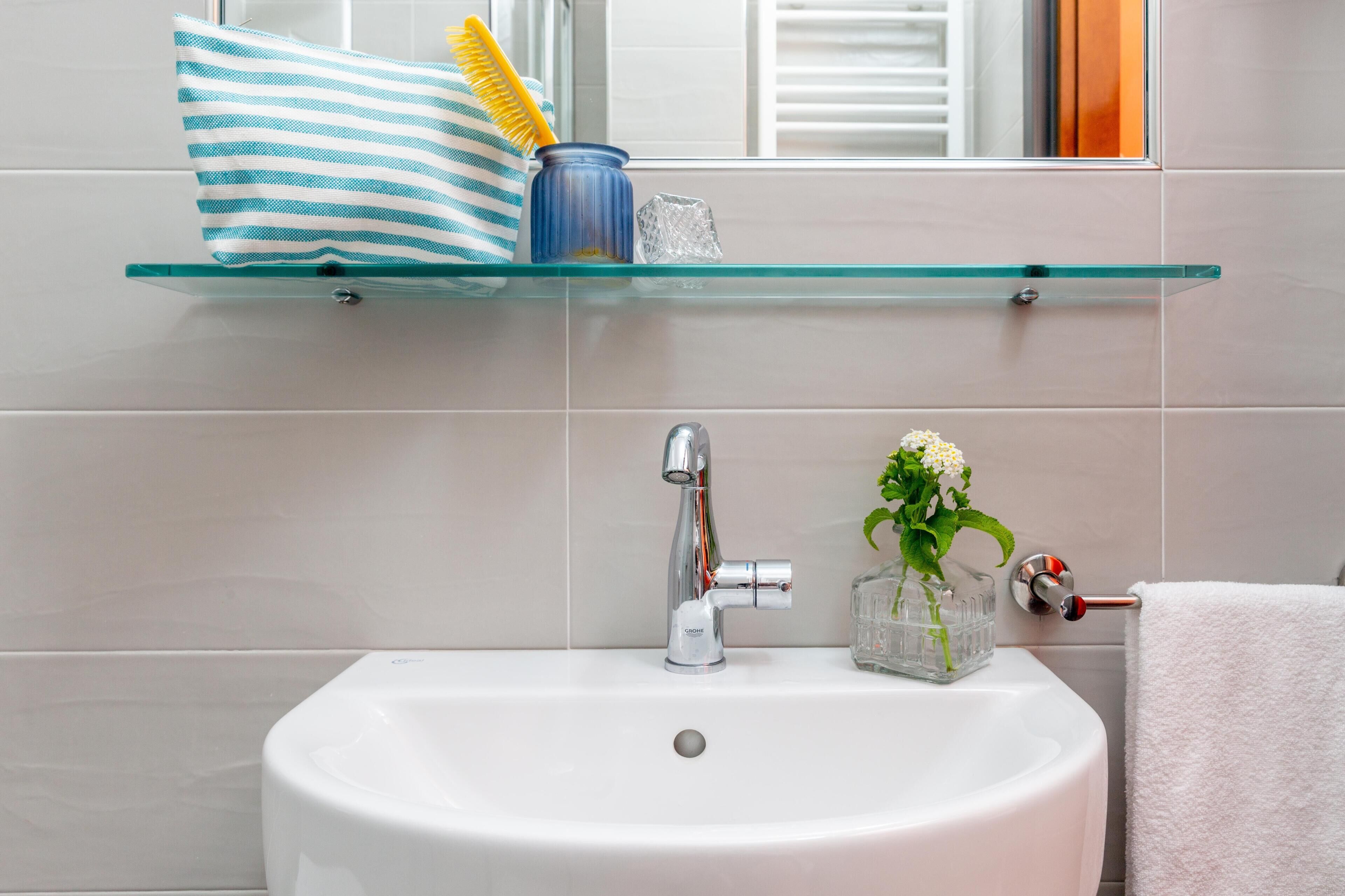 A bathroom with a white sink, a glass shelf with toiletries, and a towel rack.