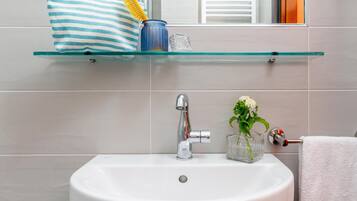 A bathroom with a white sink, a glass shelf with toiletries, and a towel rack.