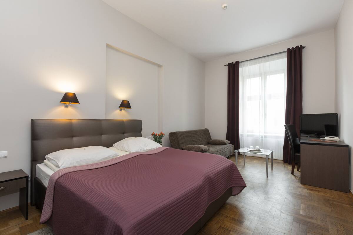 A hotel room with a bed, a desk, a chair, a TV, and a window with curtains.