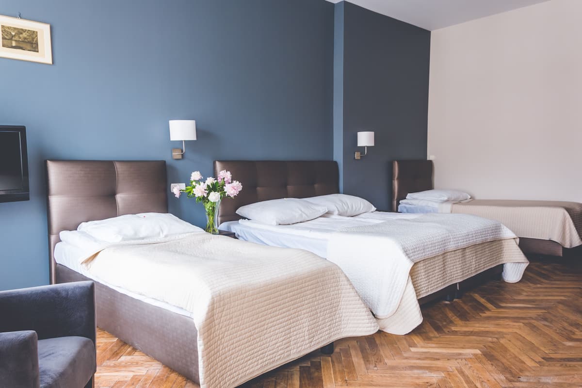 A hotel room with two beds, a wooden herringbone floor, and a wall-mounted TV.