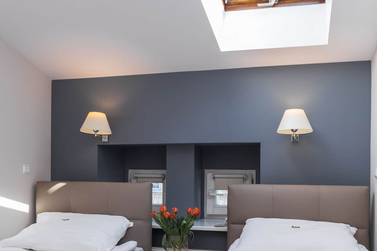 A hotel room with two beds, a skylight, a nightstand with a lamp, and a vase with flowers.