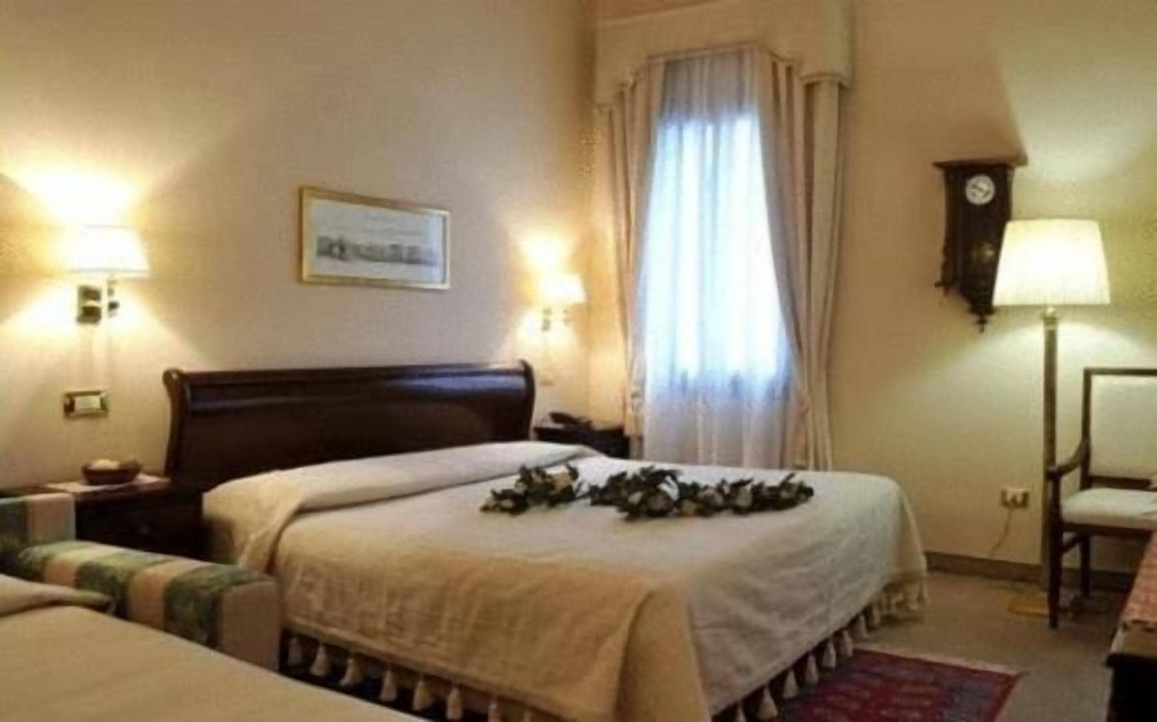 Ein Hotelzimmer mit einem großen Bett, zwei Nachttischen, einem Sessel, einer Wanduhr und einem Fenster mit Vorhängen.